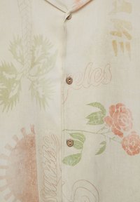 Camicia a maniche corte con bottone in tessuto beige, caratterizzata da stampe di palme e rose in verde e pesca, dotata di bottoni in legno e colletto rilassato.