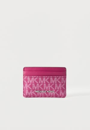 Porte-cartes rose Michael Kors avec motif logo embossé et trois emplacements pour cartes sur fond blanc.