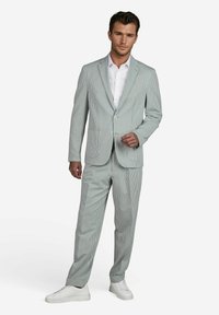 Gestreept pak in lichtgroen en wit, met een op maat gemaakt blazer met revers en bijpassende, soepel vallende broek, gecombineerd met witte sneakers.