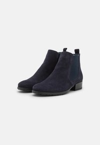 Un paio di stivali alla caviglia Chelsea in suede blu navy con pannelli elastici laterali e tacchi bassi a blocco su uno sfondo bianco.