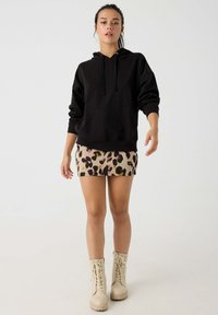 Sudadera negra con capucha y bolsillo canguro, combinada con una falda de estampado de leopardo beige. El modelo lleva botas de combate crema con cordones.