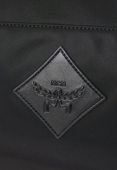 Black nylon bag featuring a raised, diamond-shaped, leather patch with embossed logo and decorative wings, contrasted by textured stitching.