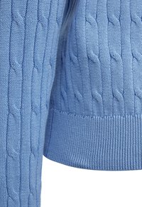 Blauwe gebreide stof met verticale kabelsteekpatronen en geribde zoom, met een close-up van de textuur van de mouw en het lichaam.