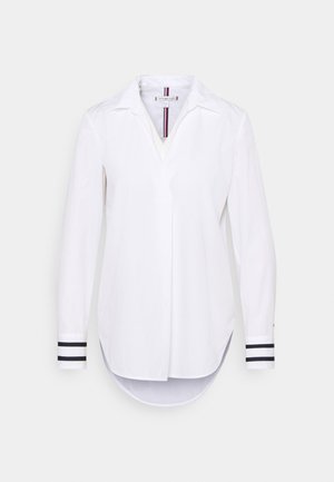 Wit shirt met lange mouwen, kraag, V-hals, afgeronde zoom en zwarte gestreepte manchetten, getoond tegen een lichte achtergrond.