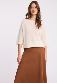 Kremowy sweter dzianinowy z szerokim dekoltem i krótkimi rękawami, połączony z brązową spódnicą midi o gładkiej fakturze i kątowych szwach.