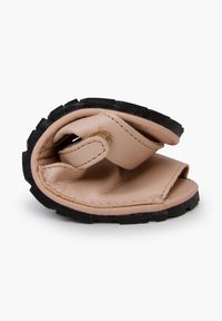 Väännetty sandaali, jossa on pehmeä beige nahka yläosa ja teksturoitu musta kumipohja. Ominaisuuksiin kuuluu minimalistinen muotoilu avonaisella varpaalla ja sivuilla.