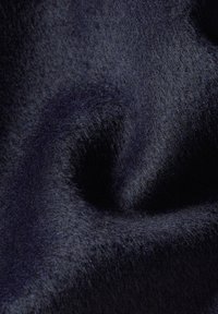 Mörk marinblått tyg med en mjuk, fluffig textur. Ytan verkar något melerad, vilket skapar visuell djup och en rik, varm känsla.