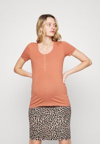T-shirt de maternidade em rust com mangas curtas, decote em forma de gota e detalhe de cinco botões; combinado com uma saia de estampado leopardo até ao joelho.