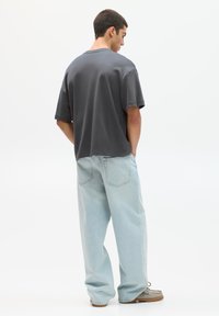 T-shirt en coton gris avec une coupe décontractée, associé à un jean en denim baggy bleu clair et des chaussures grises à texture.