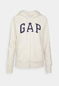 Felpa crema con zip, dotata di tasca a marsupio e logo "G.A.P." ricamato in blu sul davanti. Texture morbida, cappuccio con lacci.