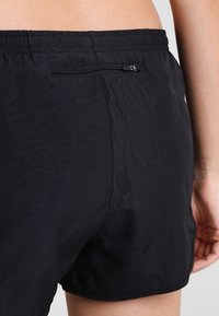 Svarta badshorts med ett texturerat mönster, elastisk midja och en zip-fick bakom för säker förvaring.