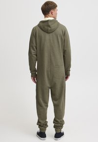 Olive green jumpsuit with a hood, made of soft fabric. Features elastic cuffs and a back pocket. Designed for a relaxed fit.