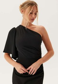 Svart one-shoulder klänning med en svävande ärm, rynkdetalj vid midjan och en slät tygtextur.