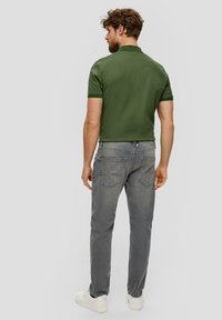 Donkergroen polo shirt met korte mouwen, gecombineerd met grijze spijkerbroek en witte sneakers; heeft een gestructureerde stof en minimale ontwerpelementen.