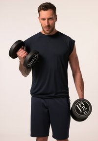 Marint träningslinne och shorts, figurnära design, lätt material. Modellen håller svarta hantlar med vit logodetalj.