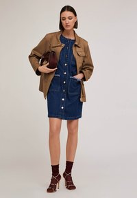 Sukienka dżinsowa z guzikami z przodu, z postrzępionymi krawędziami kieszeni, w połączeniu z brązową kurtką i burgundowymi akcesoriami. Sandały na obcasie dopełniają całość.