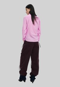 Roosa pikkade varrukatega särk sirge lõike ja nööbiga detailidega, koos vaba lõike tumepunaste pükstega, millel on lukuga taskud ja nöörid.