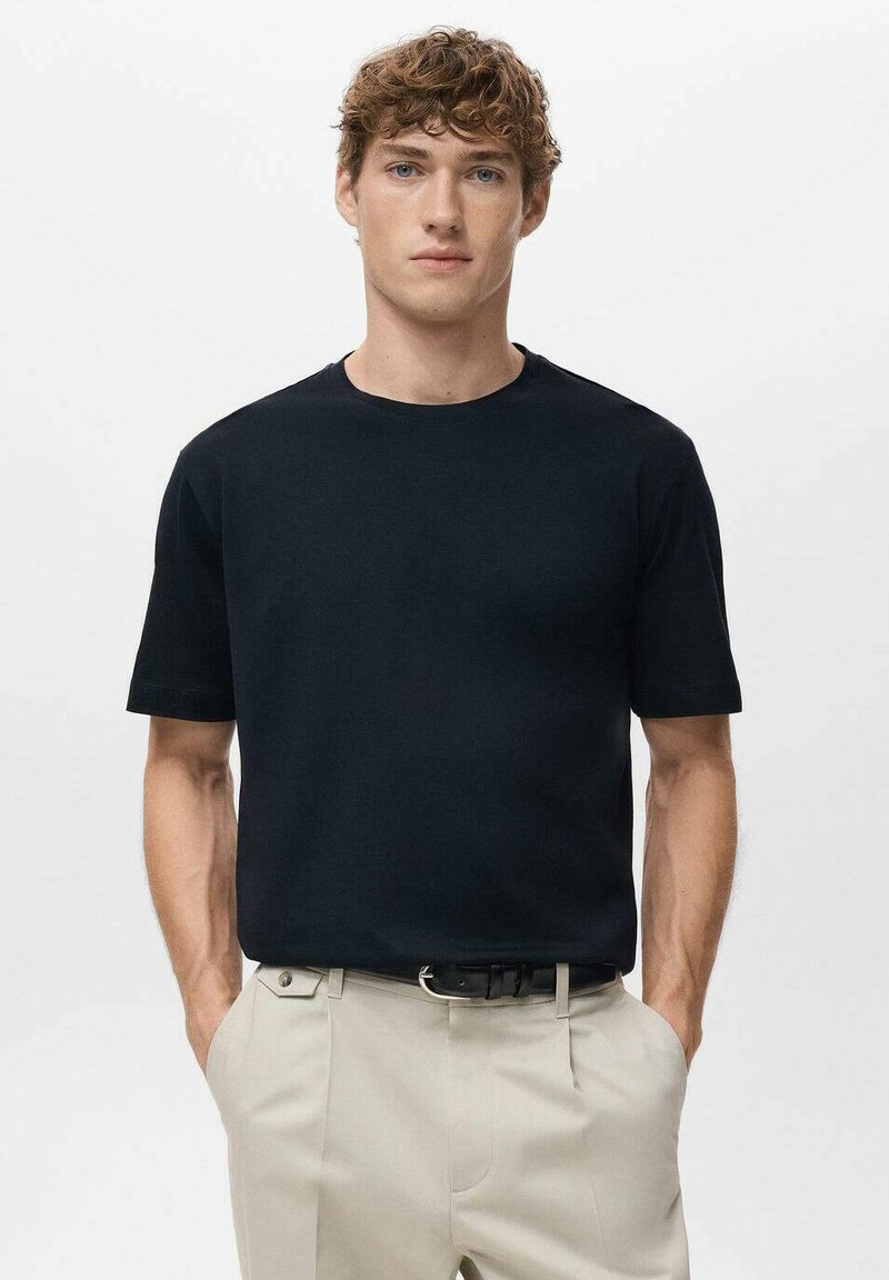 Czarny T-shirt z krótkim rękawem wykonany z miękkiego materiału, z okrągłym dekoltem i luźnym krojem, pokazany z kremowymi spodniami.