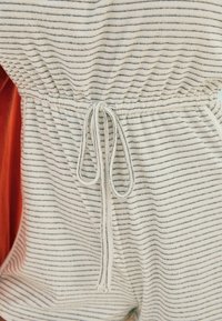 Tissu rayé blanc et bleu marine avec une taille élastique froncée et un cordon de serrage, mettant en valeur une texture en éponge et une longueur courte.