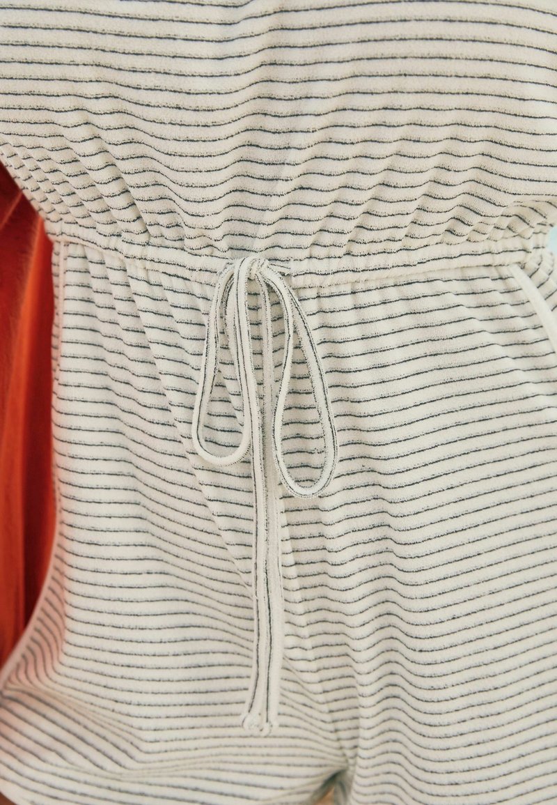 Tissu rayé blanc et bleu marine avec une taille élastique froncée et un cordon de serrage, mettant en valeur une texture en éponge et une longueur courte.