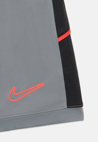 Camiseta atlética gris con detalles negros y una franja roja. Presenta el logotipo de Nike en bordado naranja. Fabricada con un tejido transpirable y texturizado.