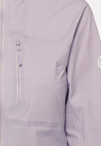 Hellviolette Jacke mit Brusttasche und vertikalem Reißverschluss sowie langem Ärmel mit weißem, rundem Logo auf dem Oberarm.