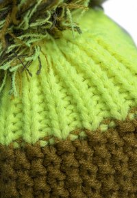 Knitted beanie with a bright lime green top and a brown ribbed base. Features textured stitches and loose yarn accents on top.