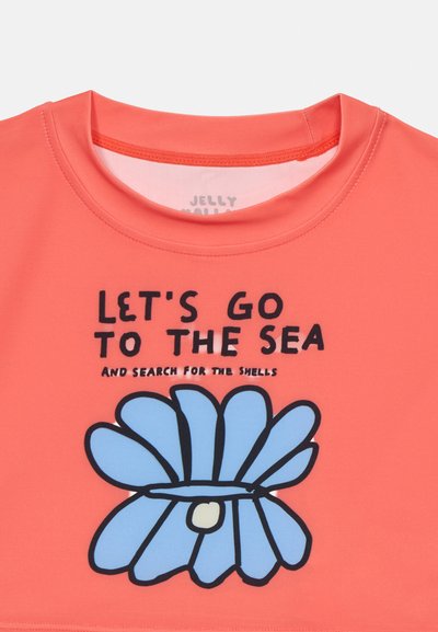 Korallfarget kortermet skjorte med rund hals som har et blått blomsterdesign og svart tekst: "LA OSS GÅ TIL HAVET OG LETE ETTER SKJELL."