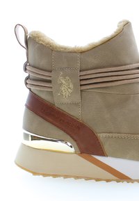 Zapatilla de deporte sintética en color marrón con acentos en tonos marrones, suave cuello de piel sintética, rayas verticales y detalle metálico en el talón. Marca "U.S. Polo Assn."