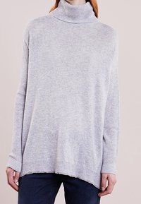 Ljusgrå polo-tröja gjord av mjukt tyg; har ribbad hals och manschetter, sänkt axelsöm och en avslappnad passform med en nederkant.