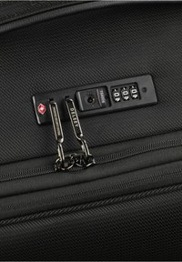 Valigia in tessuto nero con una texture, dotata di doppie cerniere nere, di un lucchetto approvato dalla TSA e di un sistema di sicurezza con combinazione.