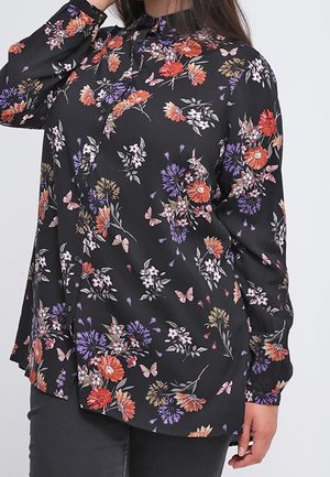 Black long-sleeve blouse with red, purple, and white floral and butterfly print, worn by a person with dark pants against a plain background.