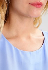 Jasnoniebieska bluzka z okrągłym dekoltem; miękka, gładka tkanina o subtelnym połysku; cechy swobodny krój i minimalne detale zszycia.