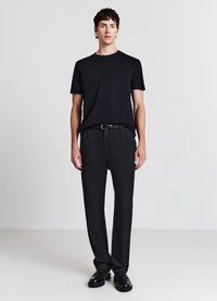 T-shirt nera a maniche corte abbinata a pantaloni eleganti scuri e scarpe stringate nere, presentando un design elegante e minimalista.