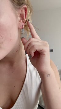 Cărămidă aurie din metal cu trei benzi spirale, asociată cu un cercei stud argintii în formă de inimă. Lobul urechii vizibil cu detalii despre textura pielii.