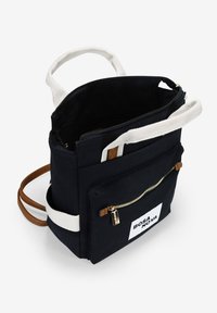 Mochila de lienzo negra con asas de tela blanca y detalles en el zipper. Presenta un bolsillo delantero con cremallera y un parche de logo. Incluye correas ajustables.