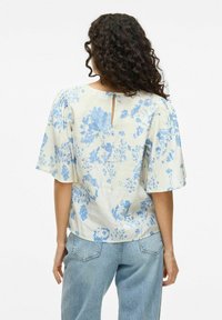 Top stampato floreale in tessuto leggero con fiori blu, maniche corte e dettaglio a chiave sulla schiena. Abbinato a denim chiaro.