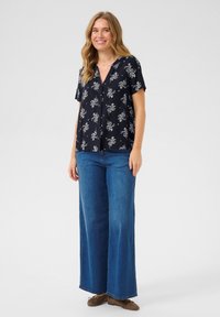 Marinblomstrad kortärmad skjorta med V-hals och knappstängning, i kombination med vida blå jeans och bruna skor. Slätt, lätt tyg.