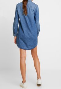 Jeansklänning i ljusblått, med knapplist fram, långa ärmar med knäppta manschetter och en rundad nederkant.