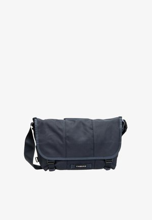 Borsa messenger Timbuk2 nera con tracolla regolabile, patta frontale assicurata da due fibbie e toppa con logo al centro davanti.