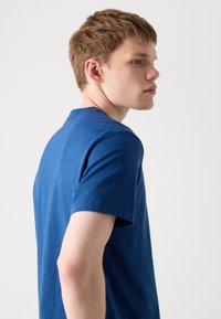 T-shirt kratkih rukava u plavoj boji od pamuka; ležeran kroj s okruglim izrezom i glatkom teksturom, prikazan na modelu sa strane.