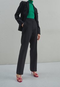 Svart skräddarsydd kavaj över en grön polotröja, i kombination med högmidjade svarta byxor och rosa remsandaler med klack.