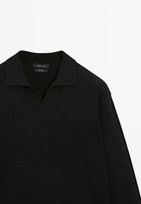 Zwarte gebreide polo trui met een v-hals, ribbelkraag en lange mouwen. Subtiele textuur, label centraal gepositioneerd bij de halslijn.