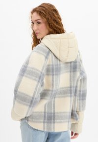 Cream and gray plaid fleece jacket with a quilted cream hood and soft texture; features wide sleeves and a relaxed fit.