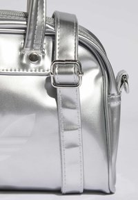 Srebrna metaliczna torba na ramię o gładkiej fakturze, z zamkiem błyskawicznym i regulowanym paskiem. Posiada logo z przodu oraz mocne szwy.