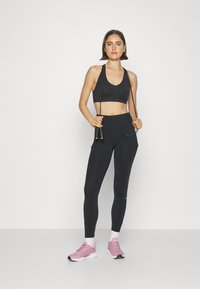 Svart sportbh och högmidjade leggings, accentuerade med fickor, tillsammans med rosa träningsskor och ett hopprep. Slät textur, kroppsformad design.