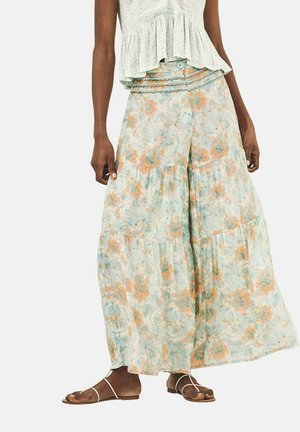 Falda de estampado floral en verde claro con acentos en naranja y azul, diseño en capas, tejido ligero, combinada con un top corto y sandalias.