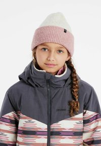 Bonnet tricoté bicolore en rose pâle et blanc, associé à une veste grise avec des accents à motifs tribaux en rose et crème.