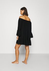 Vestito nero off-the-shoulder con maniche lunghe a campana, orlo arricciato e un tessuto leggero. Presenta dettagli testurizzati sottili.