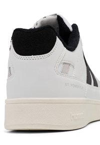 Witte leren sneaker met zwarte accenten, gestructureerde hak en rubberen zool. Heeft gestikte details en de merknaam "hummel" langs de zijkant.